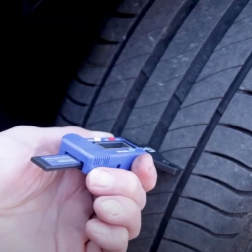 A person's hand pushes the digital tyre tread depth gauge from PCL into the tyre of a car
