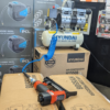 Photo from Metro Sales Surrey compressor shop showing the full set up of the Hyundai air compressor and staple gun bundle with the 8L Hyundai compressor sitting on a cardboard box with the blue coiled air hose reaching across to a seperate cardboard box which shows the coiled hose attached to a Tacwise staple gun.