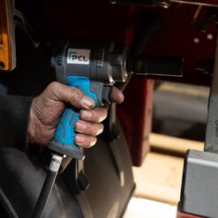 A man's hand holds the PCL Prestige stubby impact wrench in his hand as he works on a car. The image is a close up of his oil covered hand holding the impact wrench.
